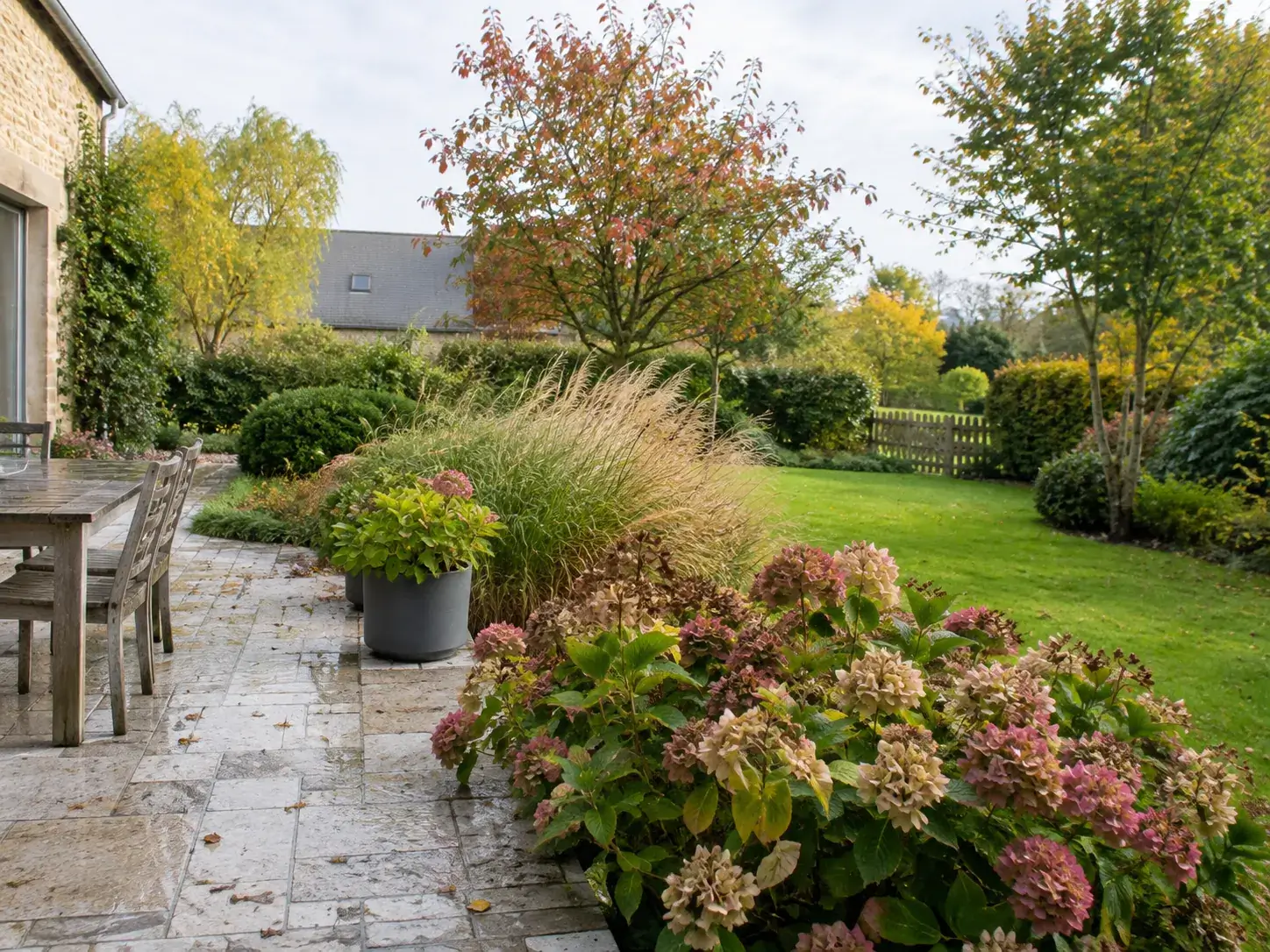 Terrasse et massifs d’un jardin en automne avec graminées, hortensias et feuillages colorés